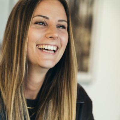 Junge Frau mit langen Haaren lacht herzlich in die Kamera.